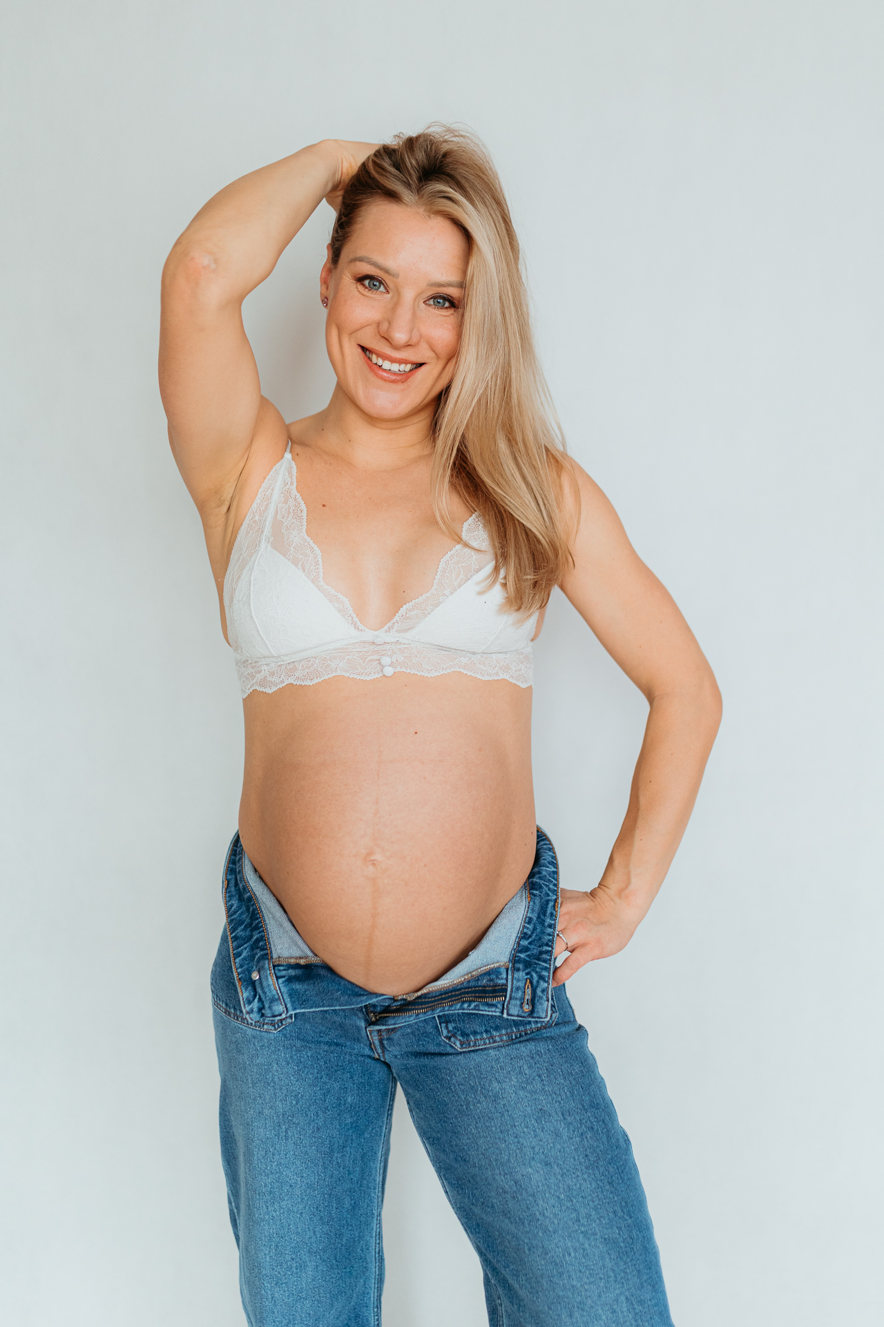 Uśmiechnięta kobieta w białym biustonoszu z odsłoniętym brzuszkiem pozuje do zdjęcia w Krakowie