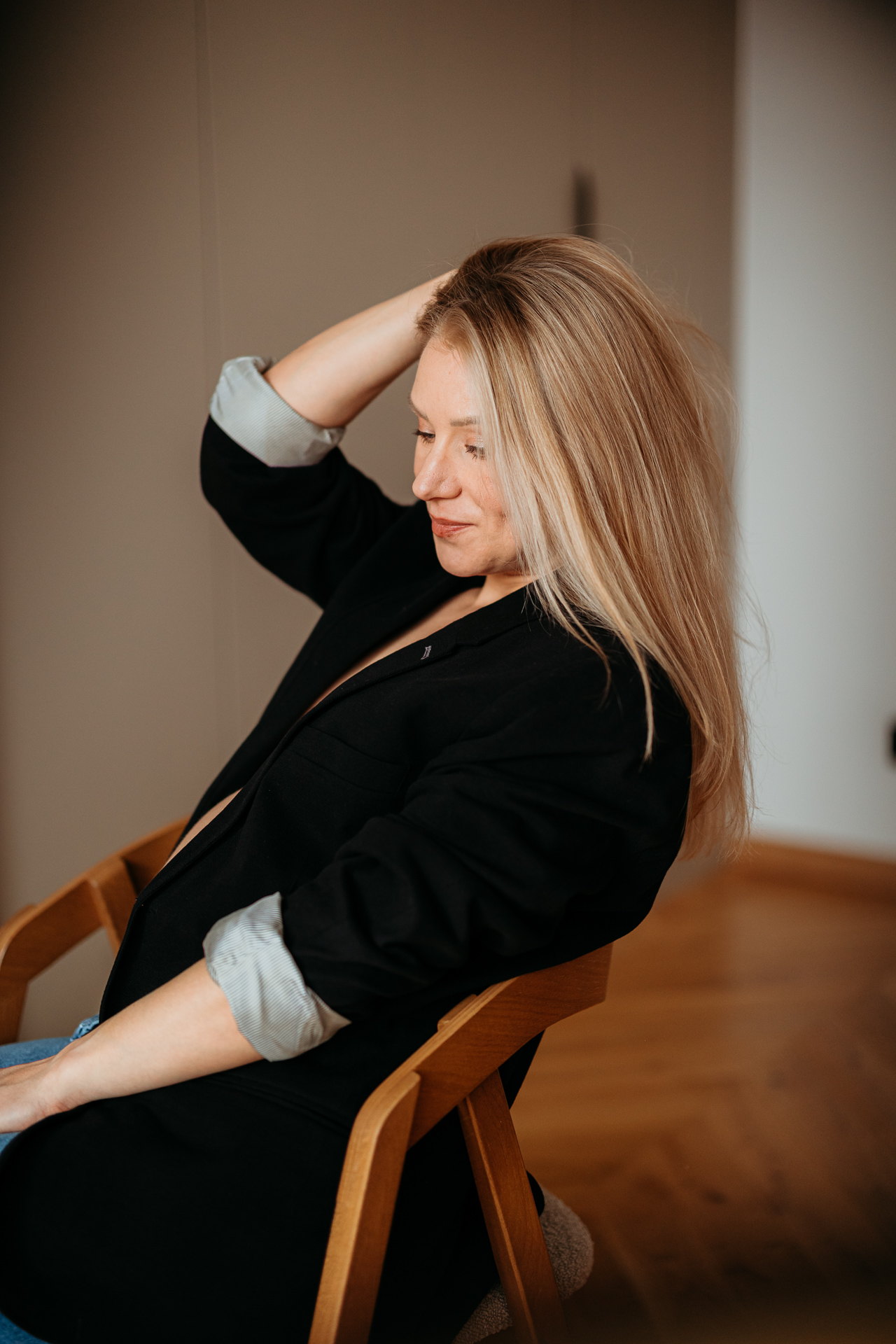 kobieta siedzi w czarnej marynarce i jeansach z odsłoniętym brzuszkiem w domu w Krakowie