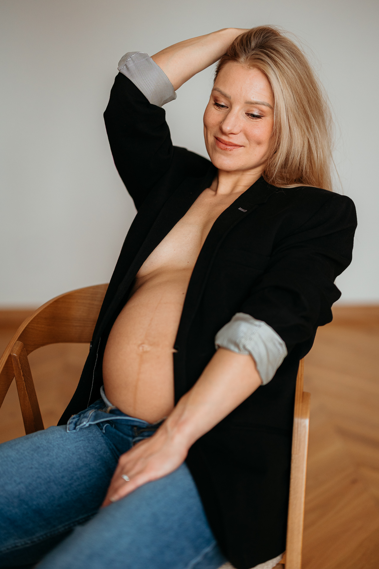 kobieta siedzi w czarnej marynarce i jeansach z odsłoniętym brzuszkiem w domu w Krakowie