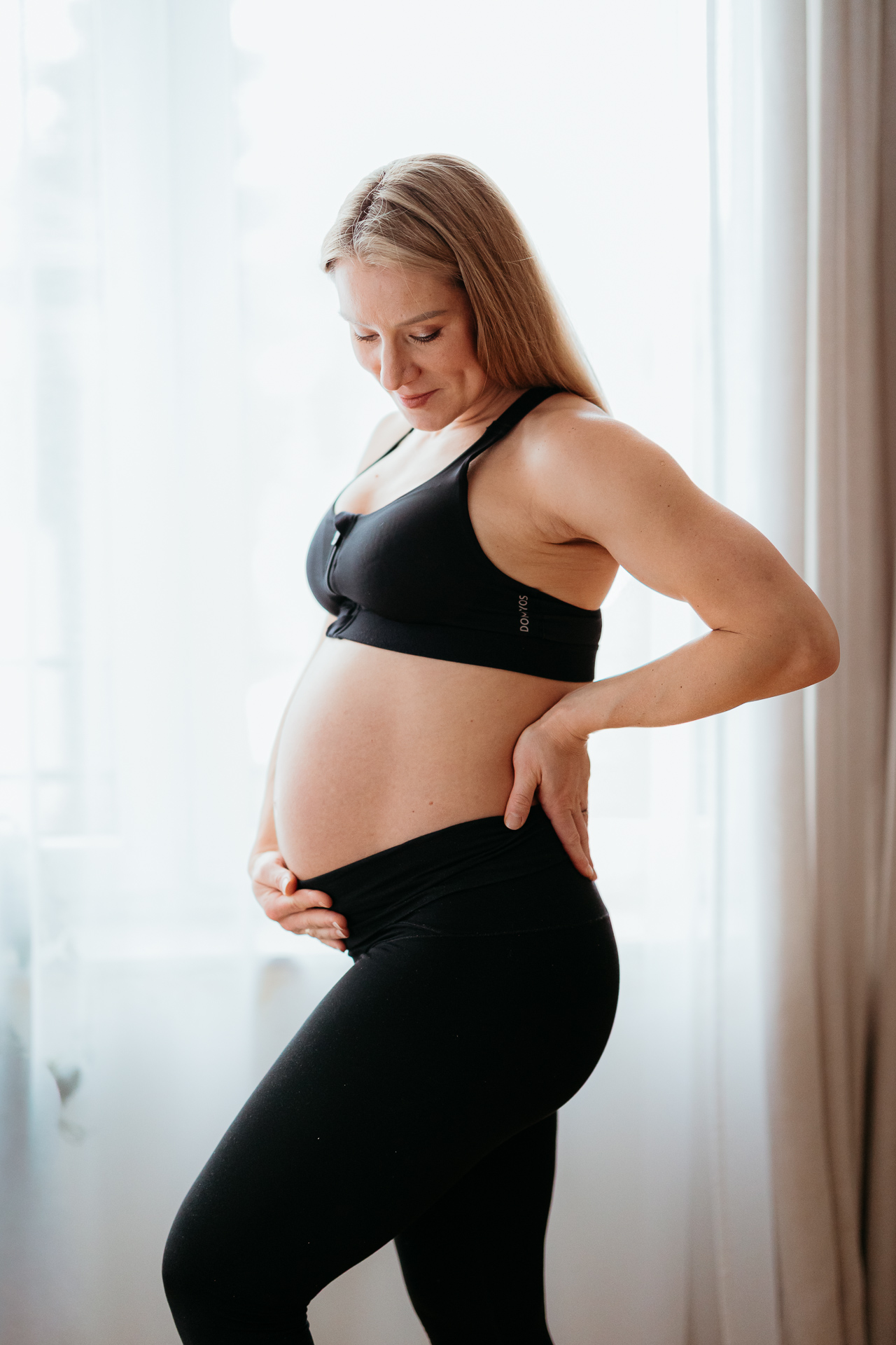 kobieta stoi przy oknie ubrana w czarne sportowe ubrania z odsłoniętym brzuszkiem w domu w Krakowie