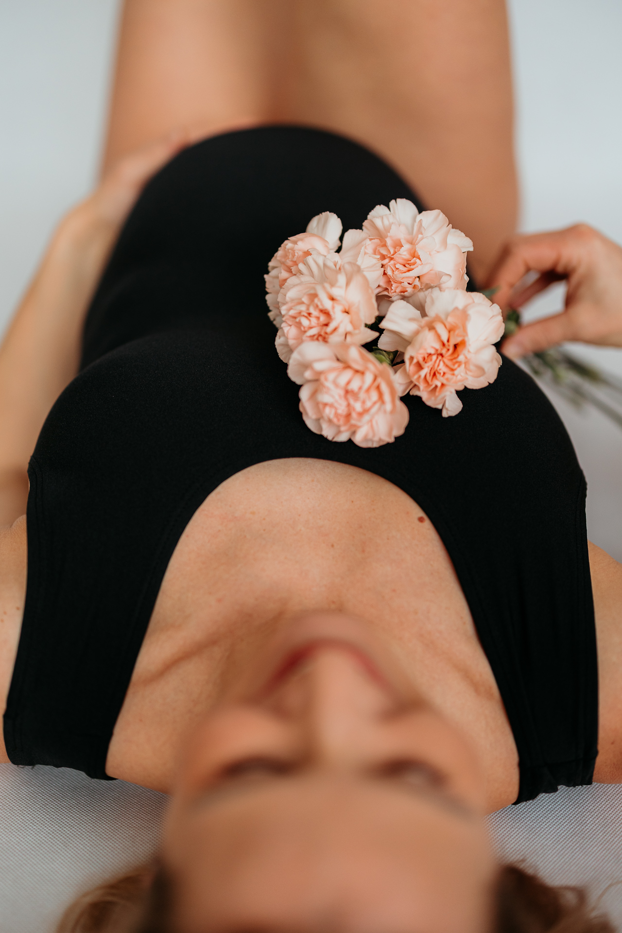 kobieta w czarnym body leży wygięta z kwiatkami w dłoni w domu w Krakowie