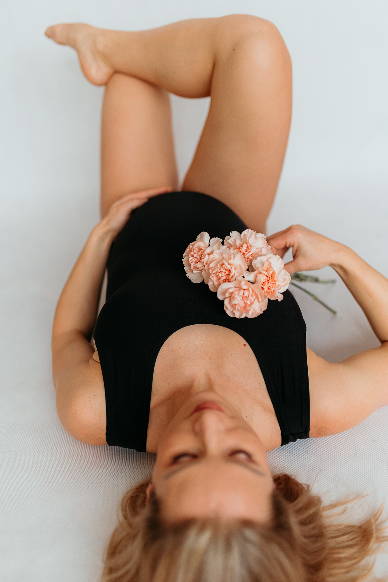 kobieta w czarnym body leży wygięta z kwiatkami w dłoni w domu w Krakowie