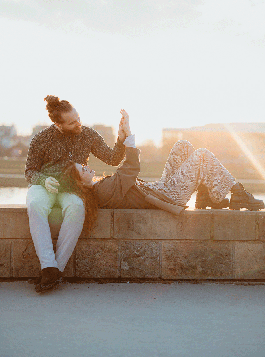 Para leży na murku i dotyka swoich dłoni, sesja miejska dla pary, Kraków, Kazimierz